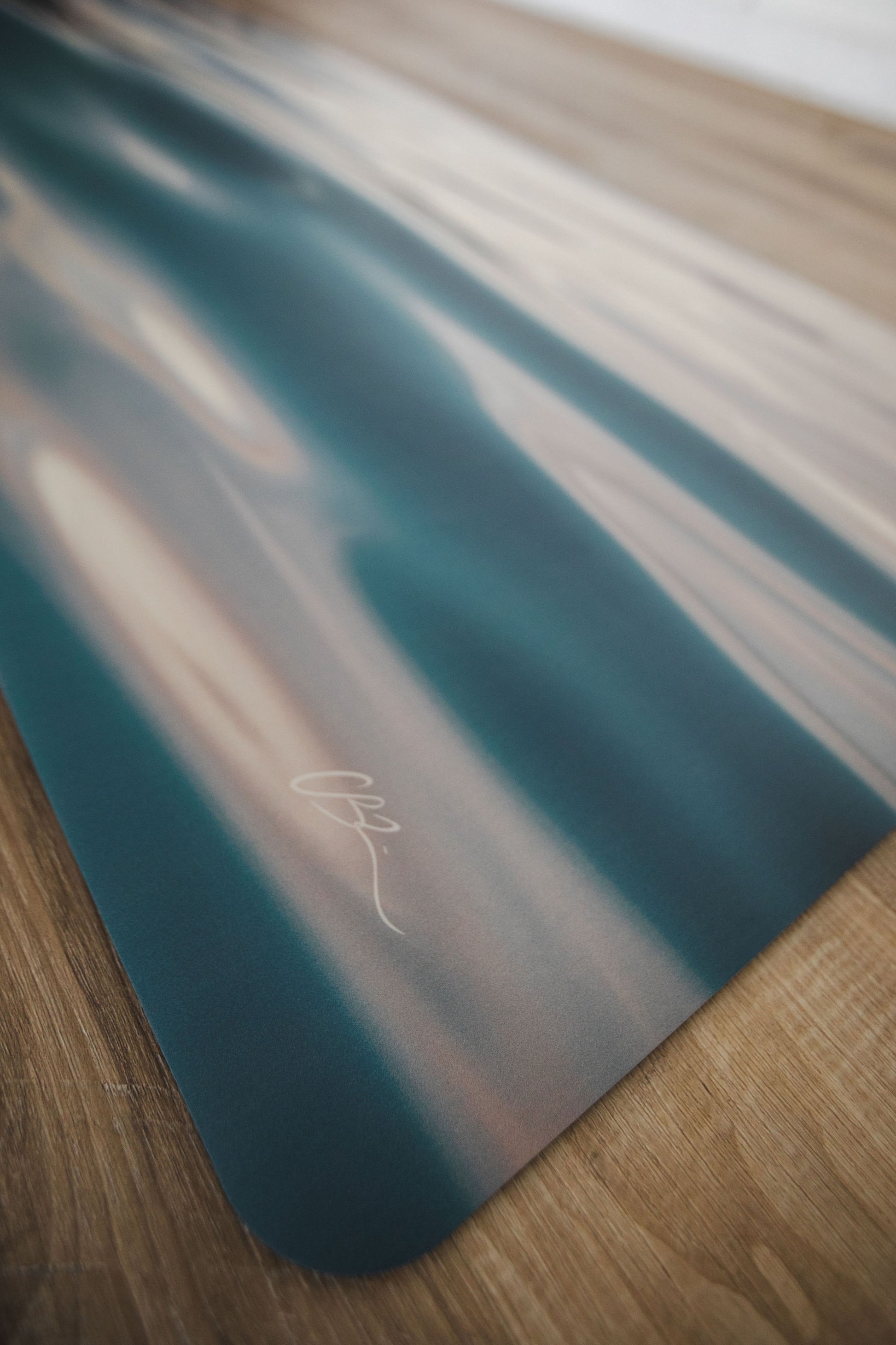 Teal yoga mat with a brand logo on a wooden floor