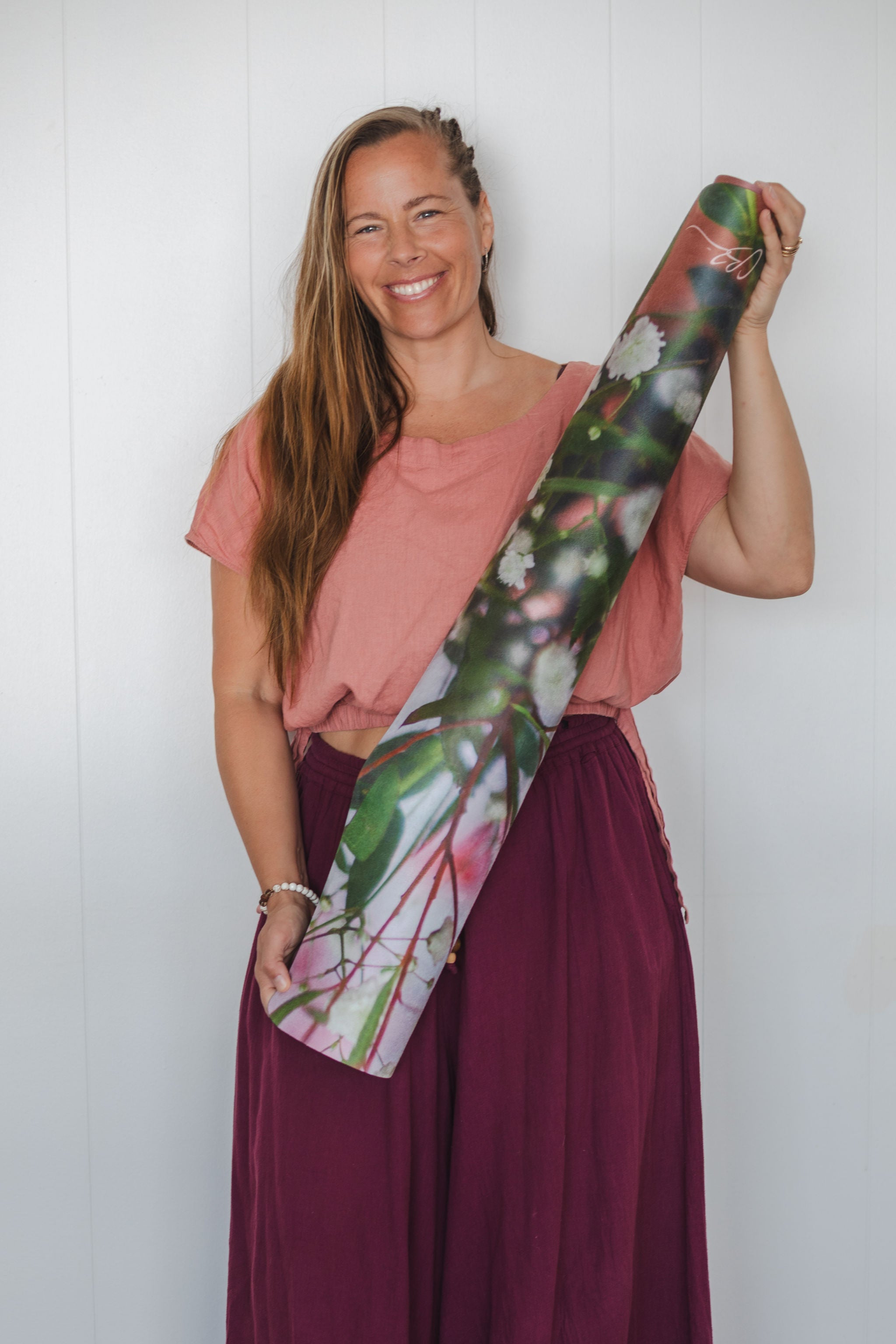 Woman holding a rolled-up yoga mat with a floral design against a white background