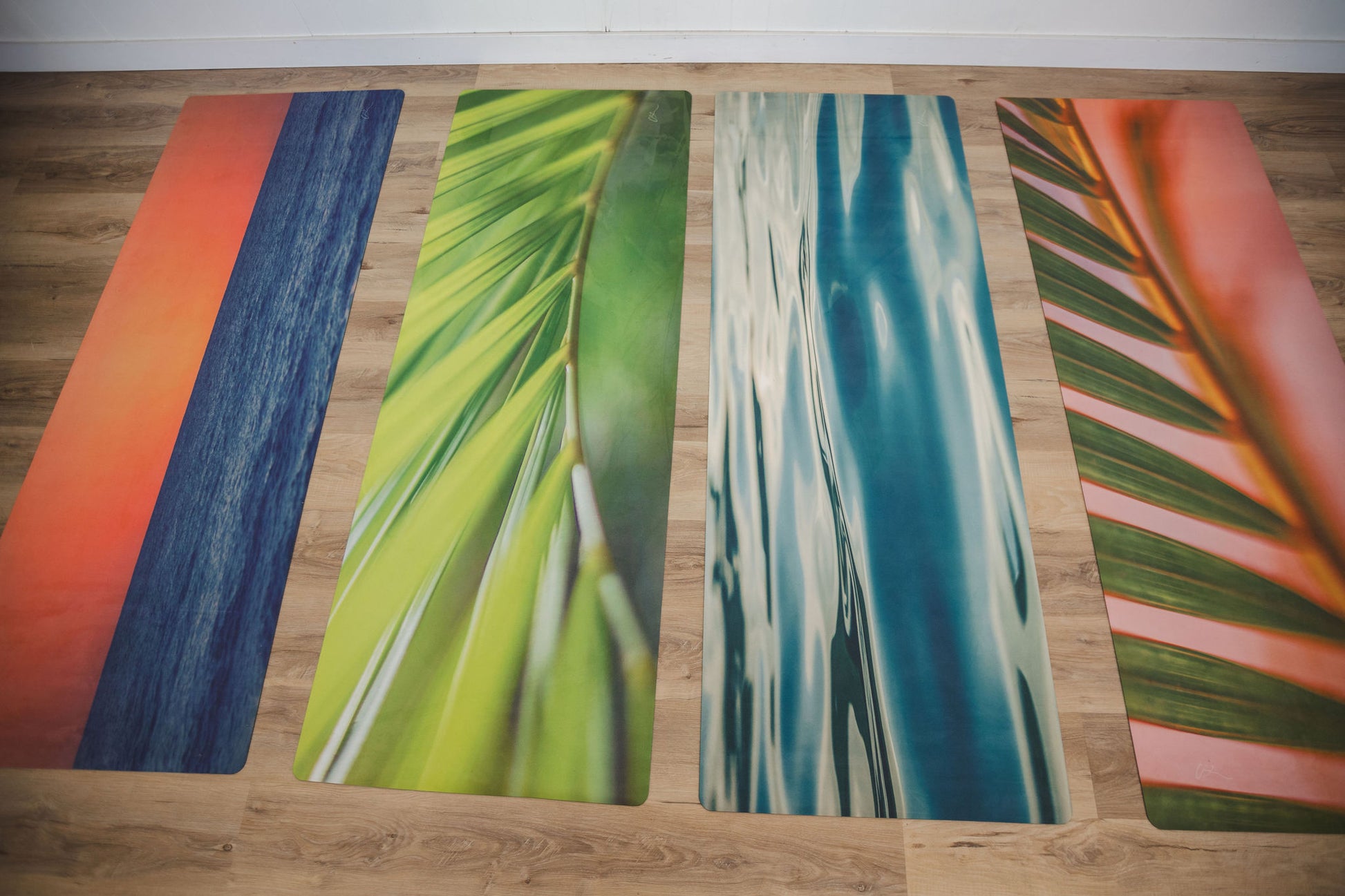 Four colorful yoga mats with nature-themed designs on a wooden floor.