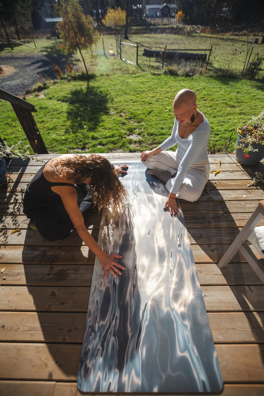 Two people sitting on a wooden deck with a large piece of paper between them, outdoors.