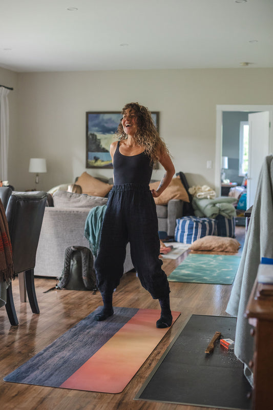 Woman in a dark outfit standing on a colorful mat in a living room.