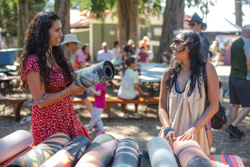 Two women at a music festival with instruments and a crowd in the background