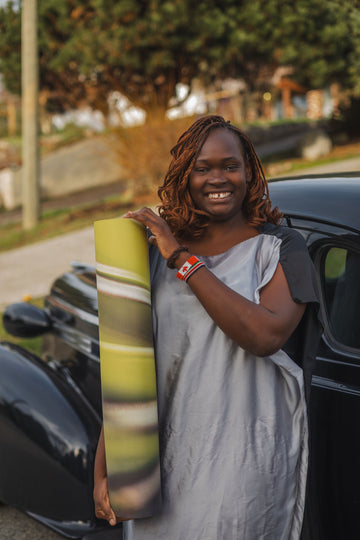 Woman holding a green and yellow striped yoga mat next to a car outdoors.