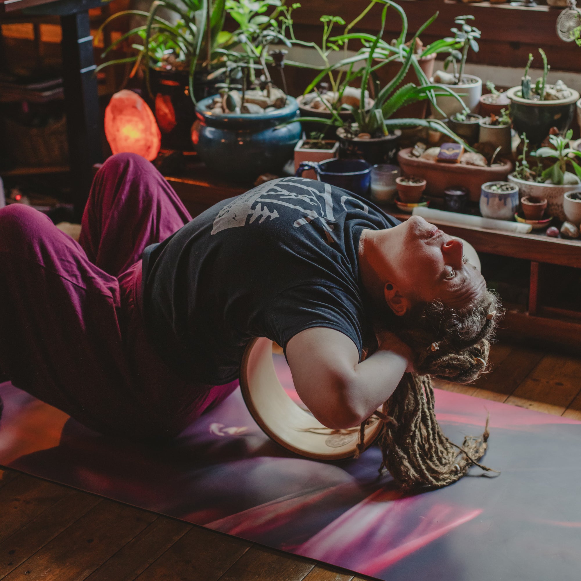 Person practicing yoga in a room with potted plants and a glowing pink light.