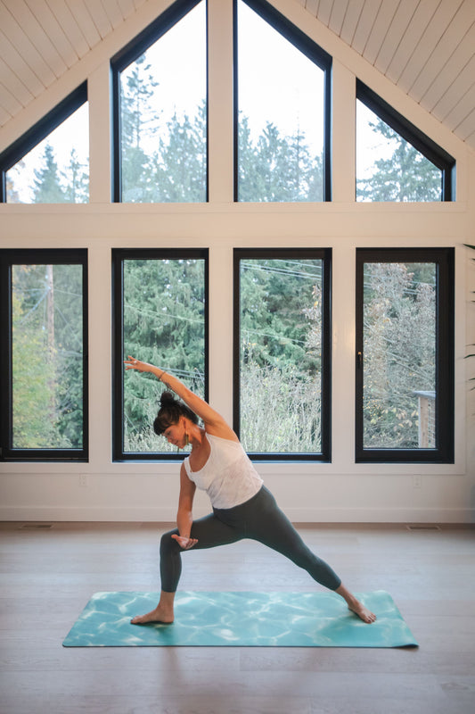 Person practicing yoga in a room with large windows showing trees outside