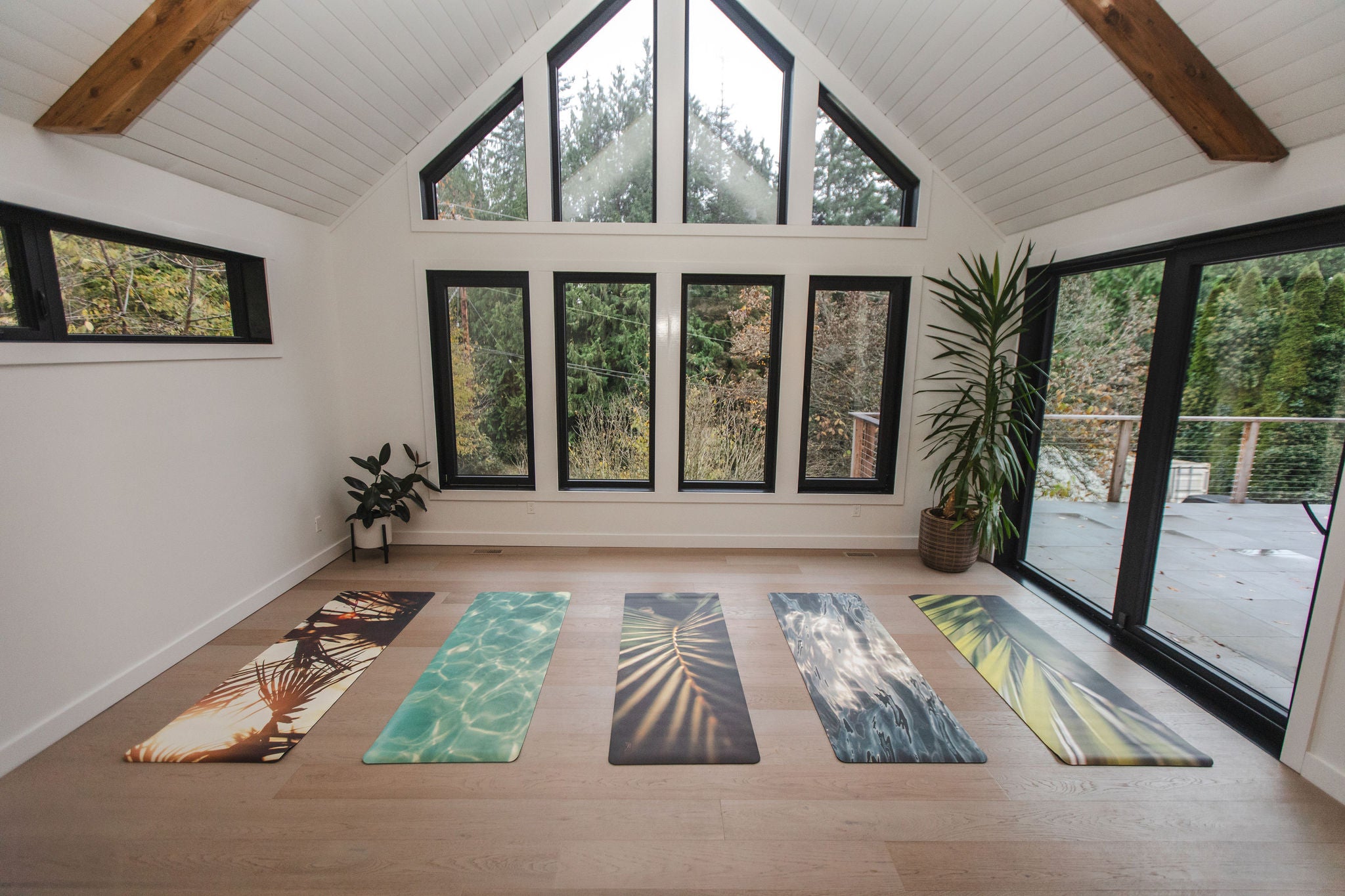 Yoga room with various yoga mats on a wooden floor and large windows.