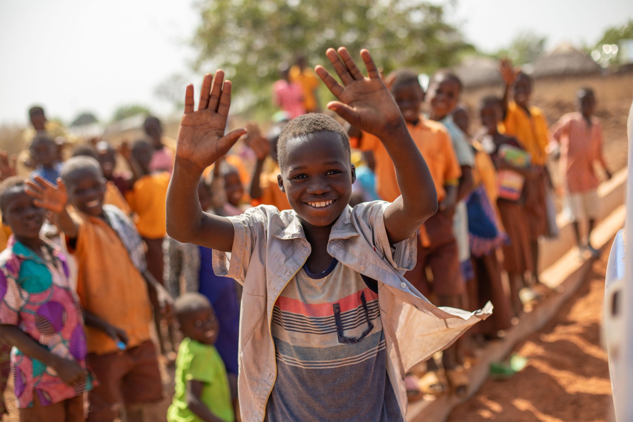 Child waving with a group of children in a rural setting