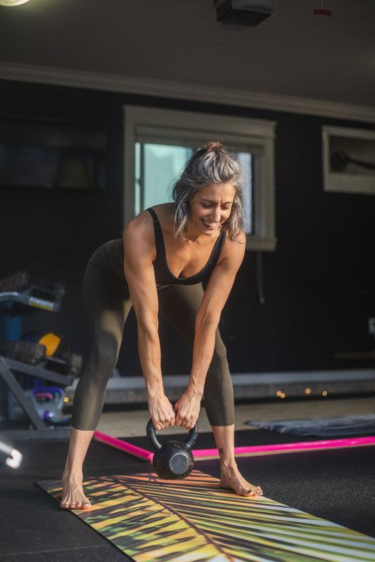 Woman exercising with a kettlebell on a colorful mat in a gym.