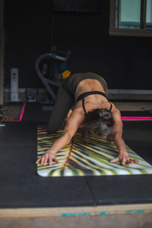 Person practicing yoga on a mat with a palm leaf design in a home setting.