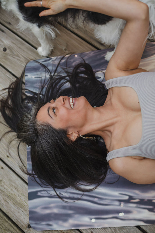 Woman lying on a wooden floor with a dog, wearing a sleeveless top.
