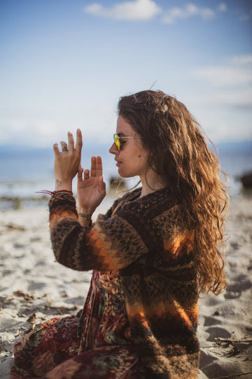 Woman sitting on a beach with ocean view, wearing sunglasses and a patterned outfit.